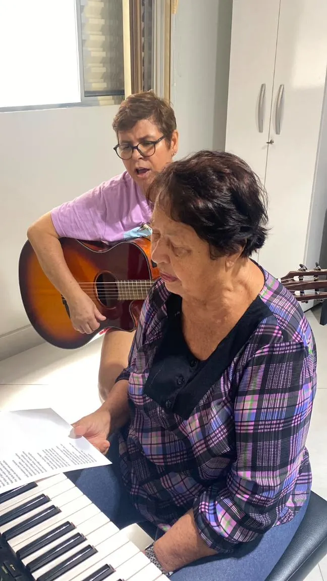 Aluna da melhor idade em aula de canto acompanhada pela professora ao violão na Spasso Musical